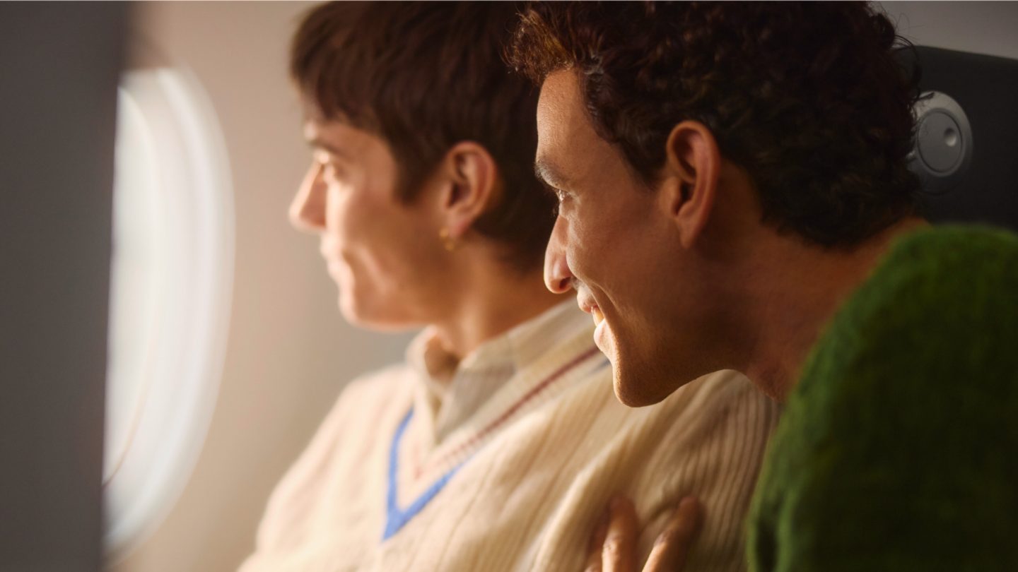 Two people smile and look out of an aircraft window.