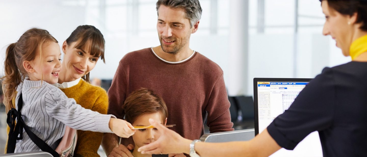 Family gathers around a laptop with a woman holding a yellow paper.
