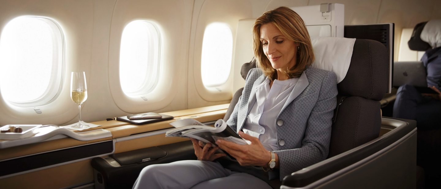 Woman reading a magazine in First Class with a glass of champagne next to her