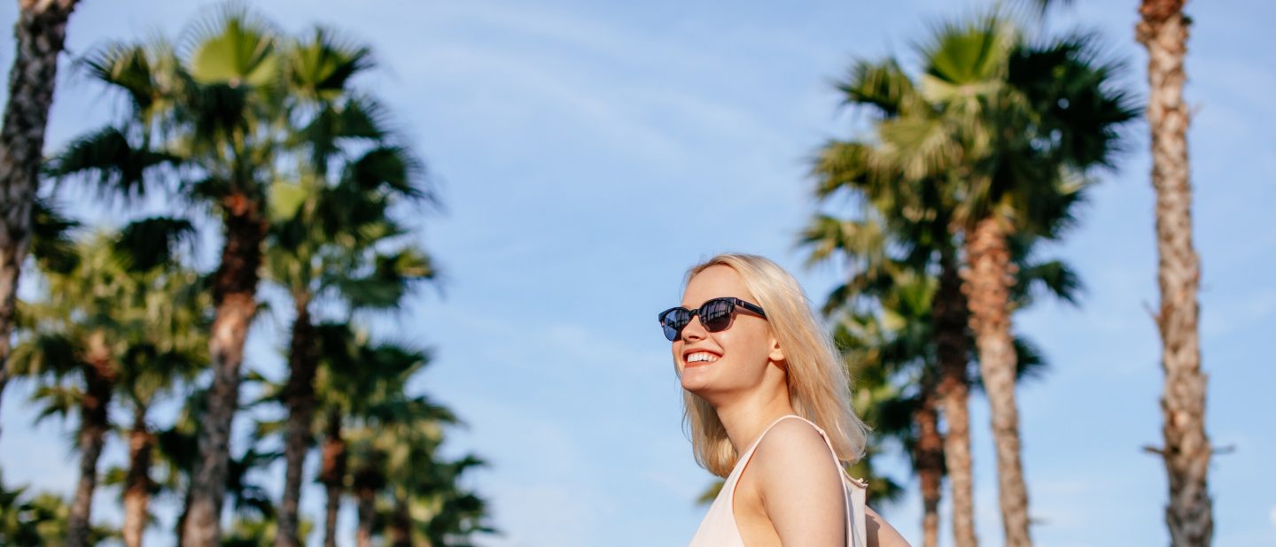 Woman enjoys a sunny day on holiday with an avenue of palm trees in the background.