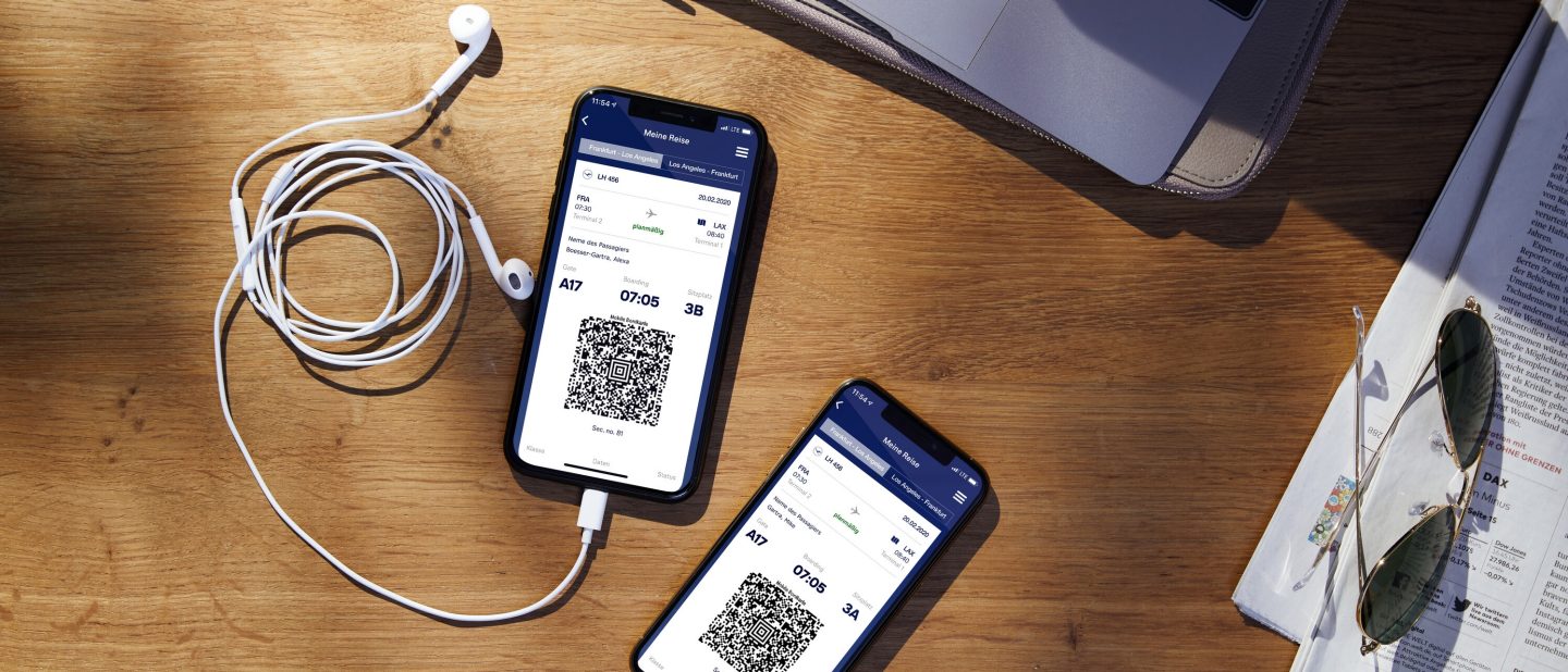 Two smartphones with QR codes sit on a table with headphones, a laptop, a magazine, and sunglasses.
