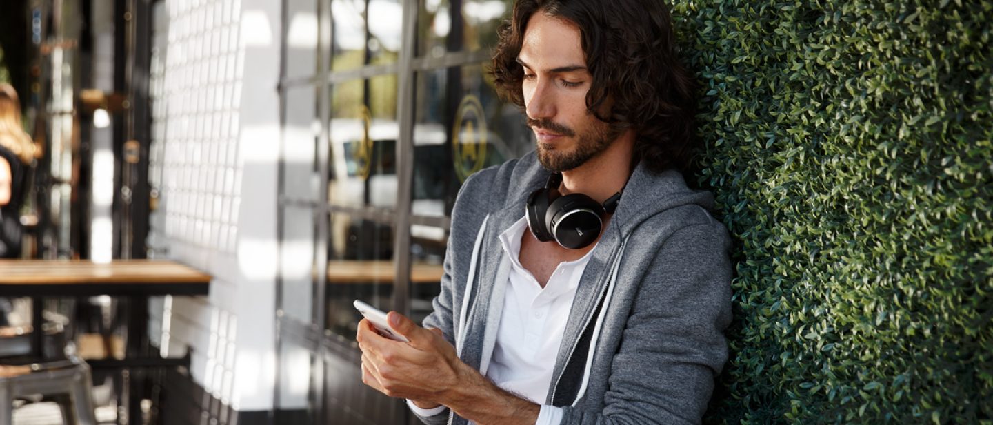 Young man with smartphone in his hand. He is using the online Chat Assistant who is helping him with a concern about his trip.