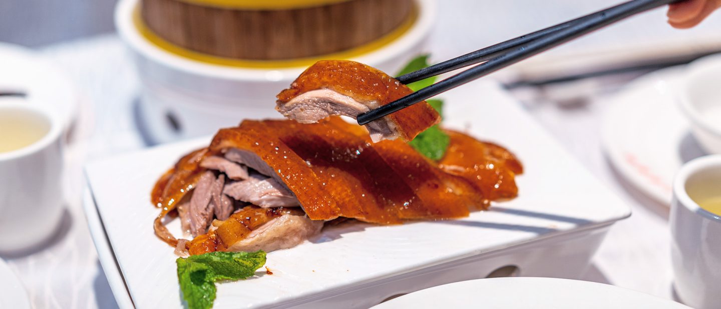 Chopsticks lifting a piece of crispy duck from a serving platter.