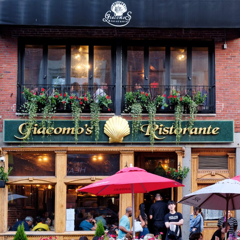 The facade of Giacomo’s Ristorante in Boston with guests and red umbrellas