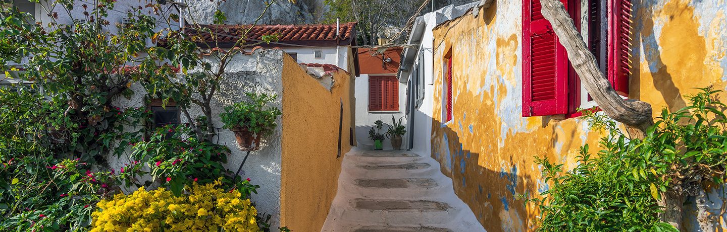 Picturesque alley in the Anafiotika neighborhood of Athens with colorful house façades, red shutters, and blooming plants – a typical example of the charming old-town atmosphere at the foot of the Acropolis.