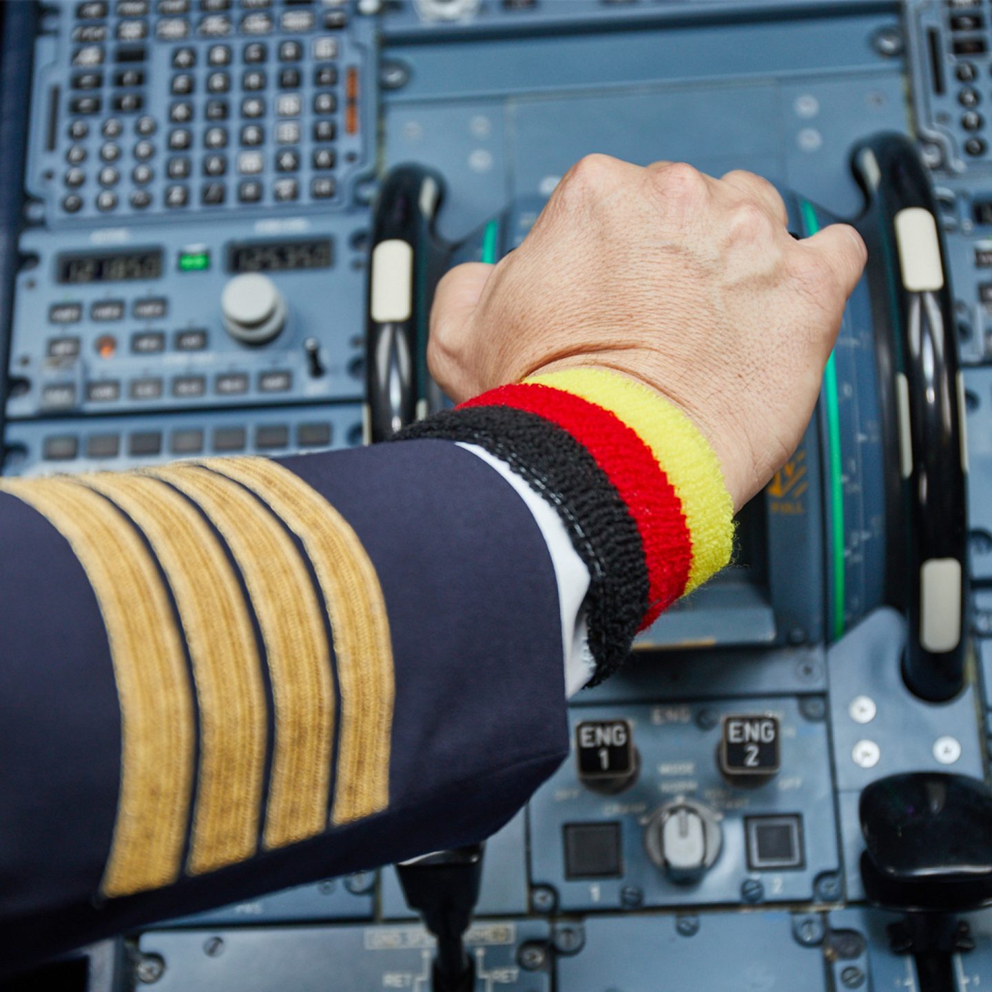 A pilot's hand on the controls of an aircraft, wearing a wristband in the colors of the German flag.