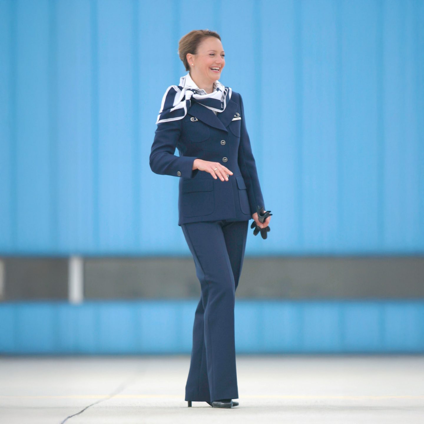 Flight attendant in navy pantsuit with scarf and neckerchief, part of a 1980s Lufthansa uniform.