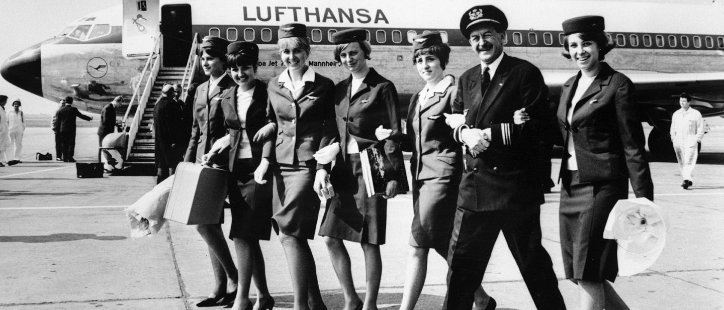Historic Lufthansa crew with pilot and flight attendants walk in front of an aircraft.
