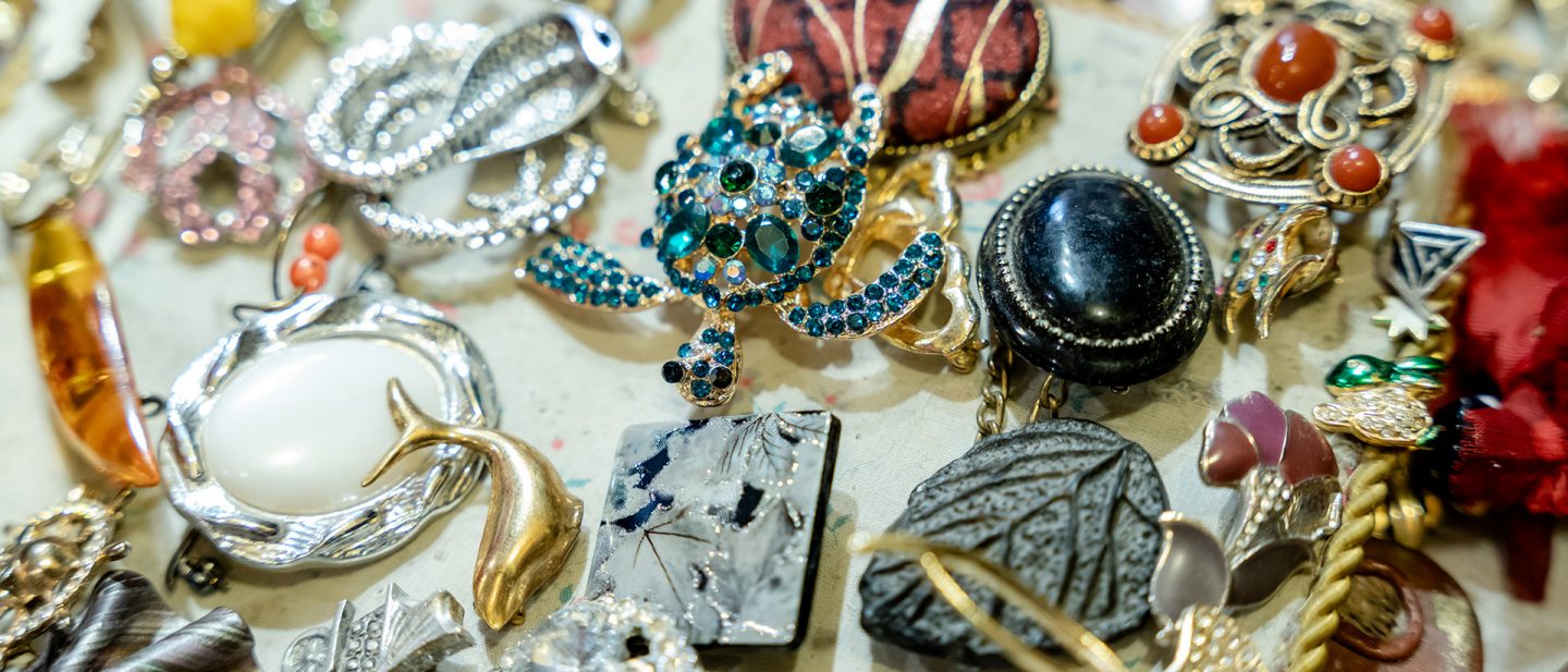 A variety of colorful vintage brooches and jewelry pieces on a textile surface