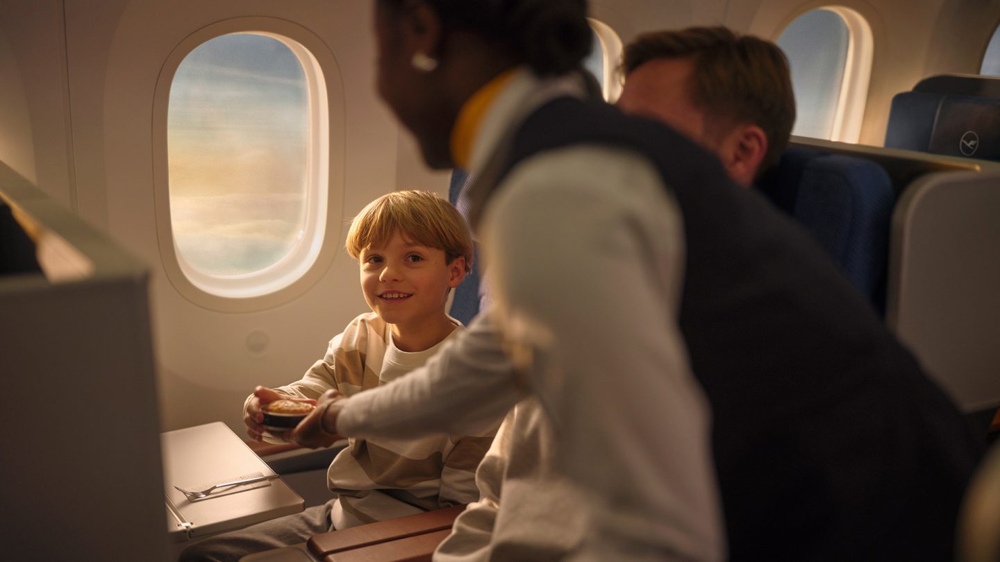 Child on airplane receives a pastry from a flight attendant at a window seat.