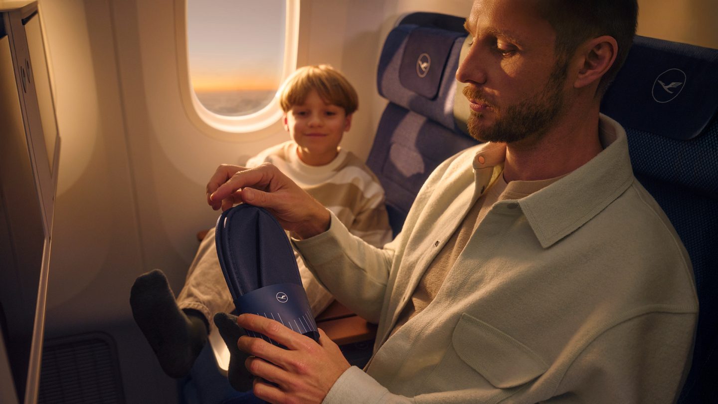 Man holds slippers in premium economy, child sits beside him.