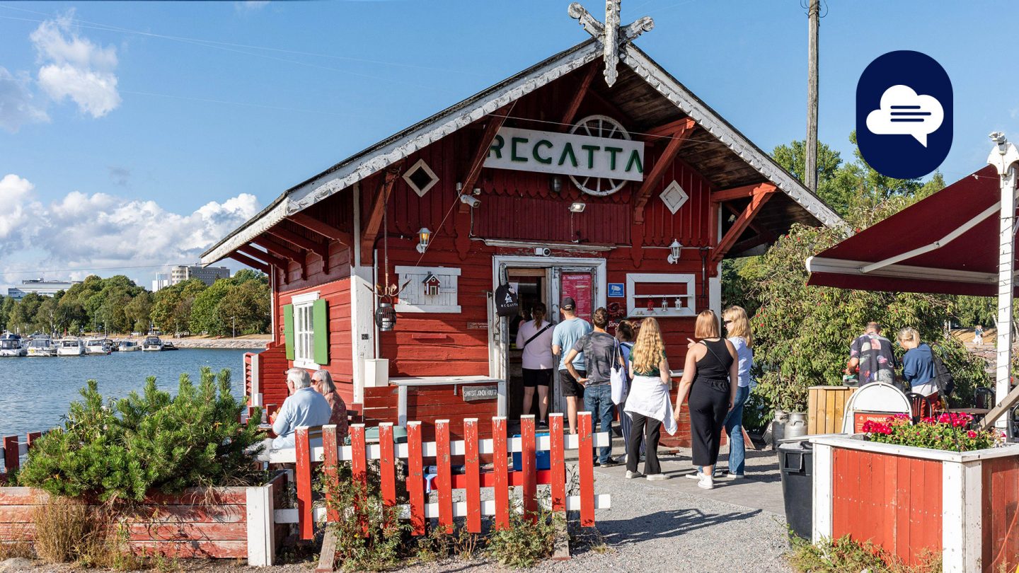 People visiting a quaint red wooden cafe named Regatta by the waterfront on a sunny day.