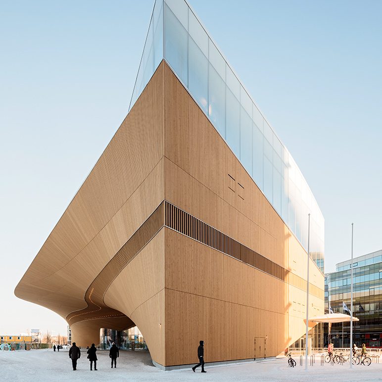 The curved architecture of the Oodi library with large windows; pedestrians nearby.