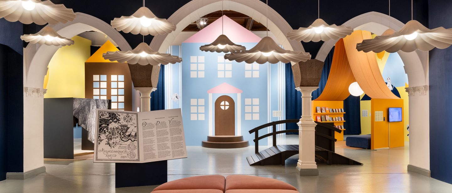 Scene from the Moomin exhibition at the Architecture and Design Museum in Helsinki with arches, colorful house facades, and playful lighting.