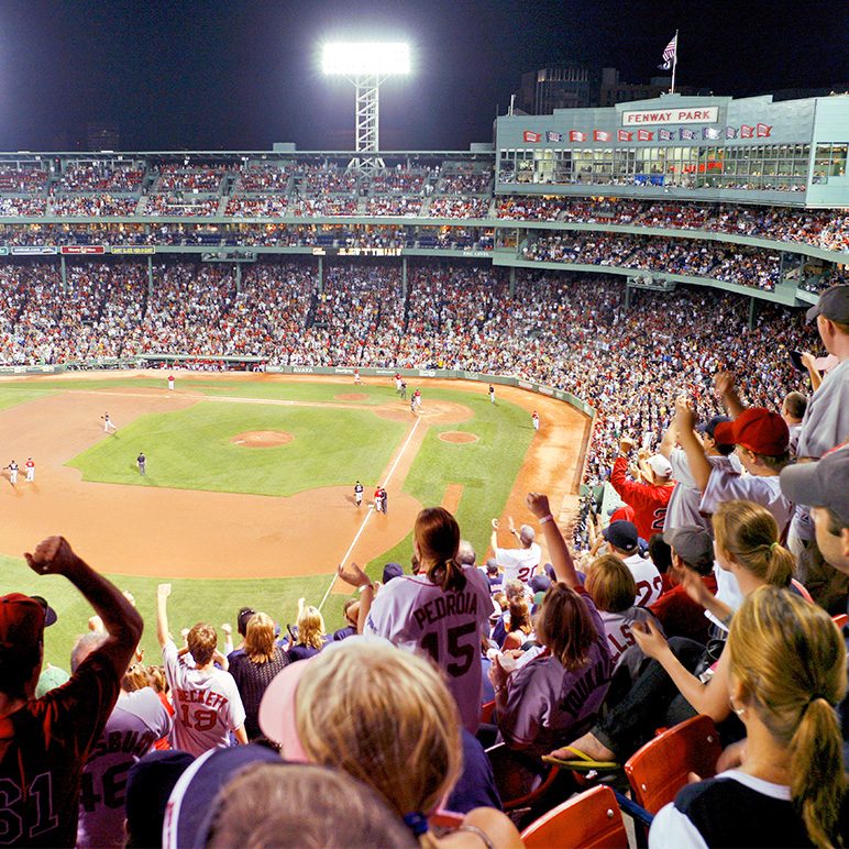 A crowded baseball stadium at night with cheering fans in the foreground