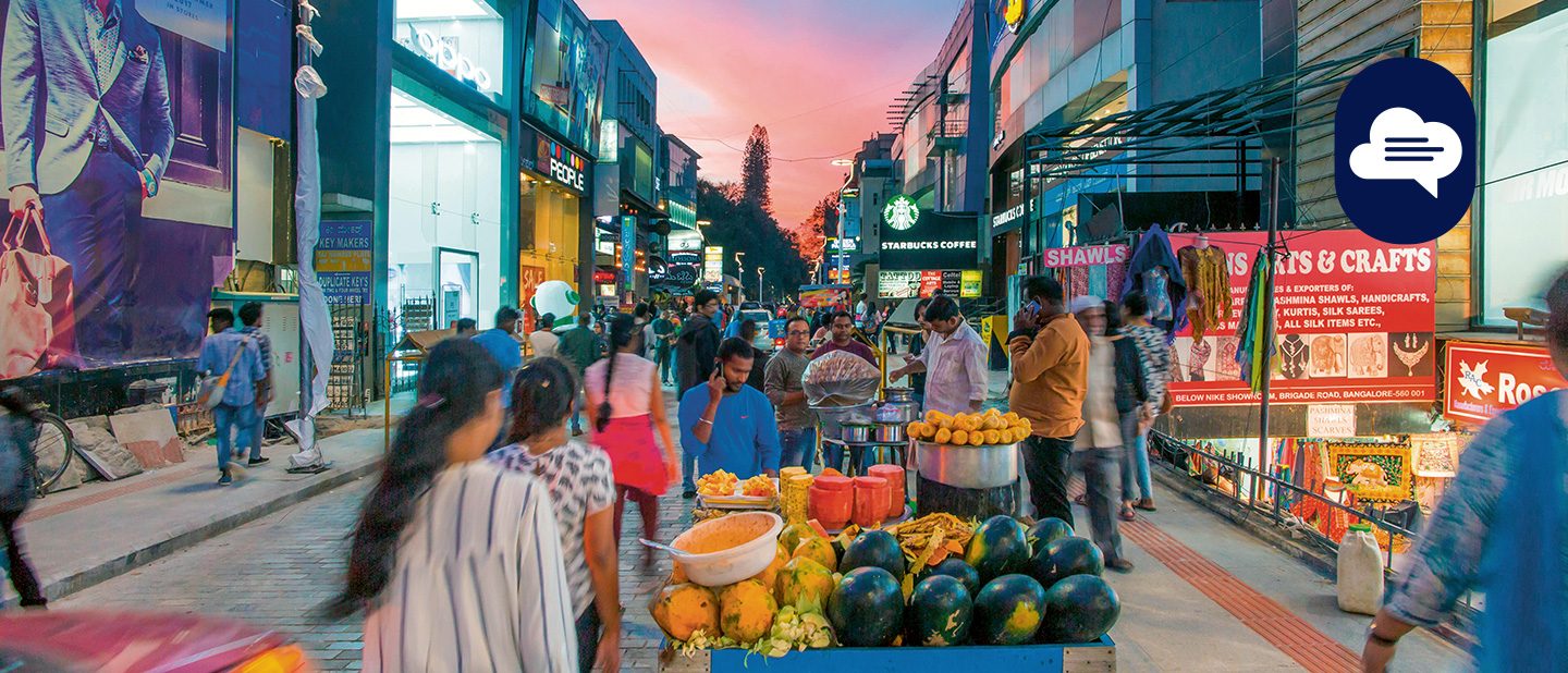 Team Stories: A bustling street market at dusk with people, shops, and fruit stalls.