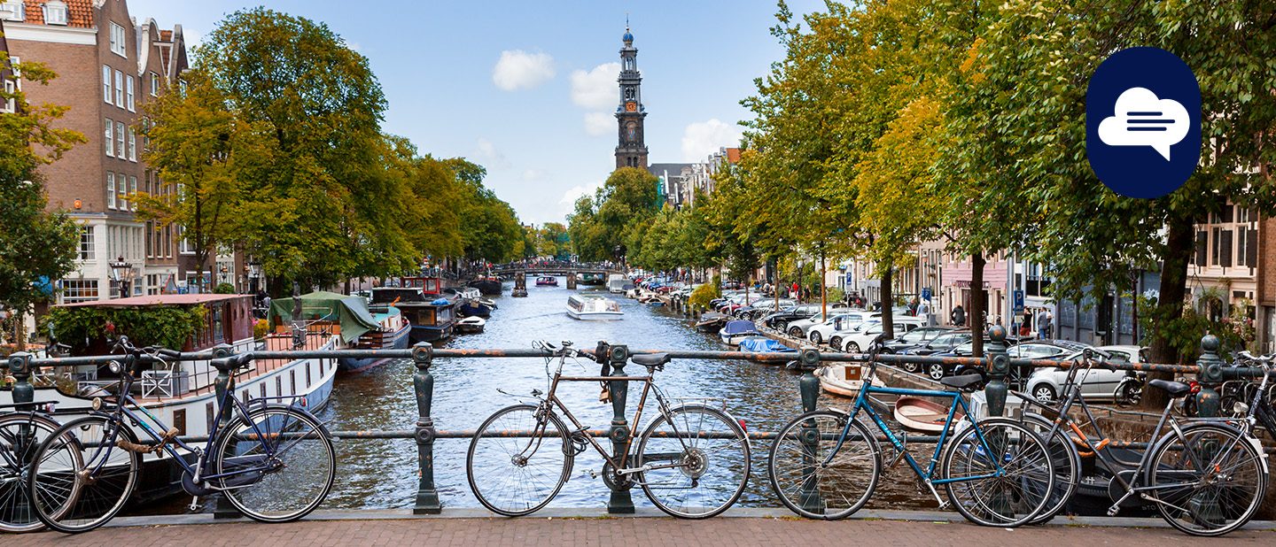 Team Stories: View of a canal in Amsterdam with bicycles leaning against a bridge railing in the foreground.
