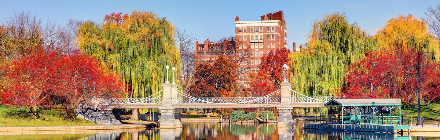 Autumn atmosphere in the Boston Public Garden with a historic bridge, vibrant fall foliage, and reflections on the water.
