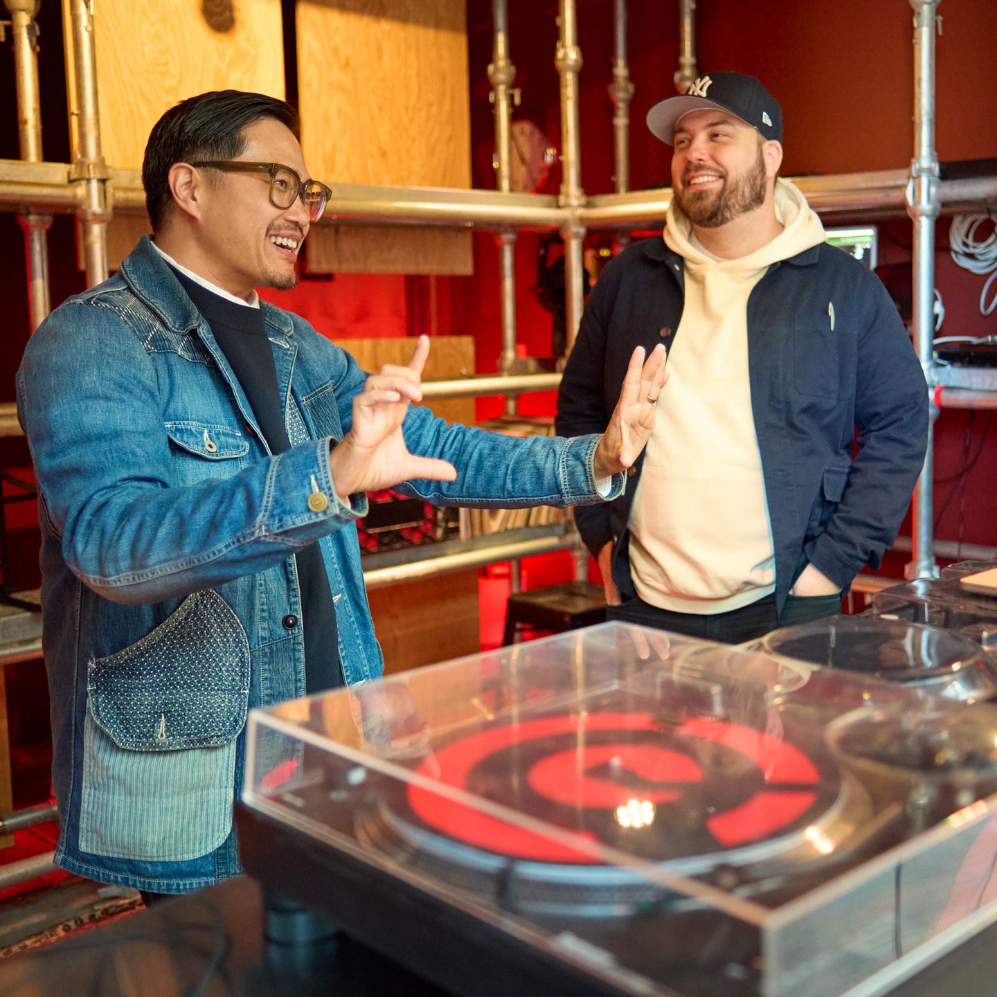 Oliver Mak gestures and smiles next to a man by a turntable